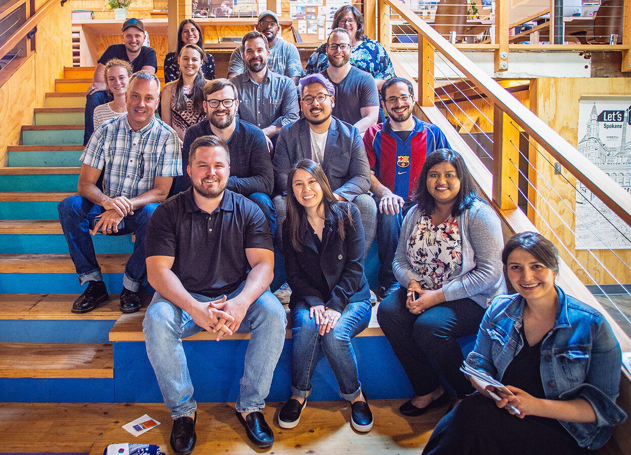 Drawn team posing together on a wooden staircase, smiling for a group photo