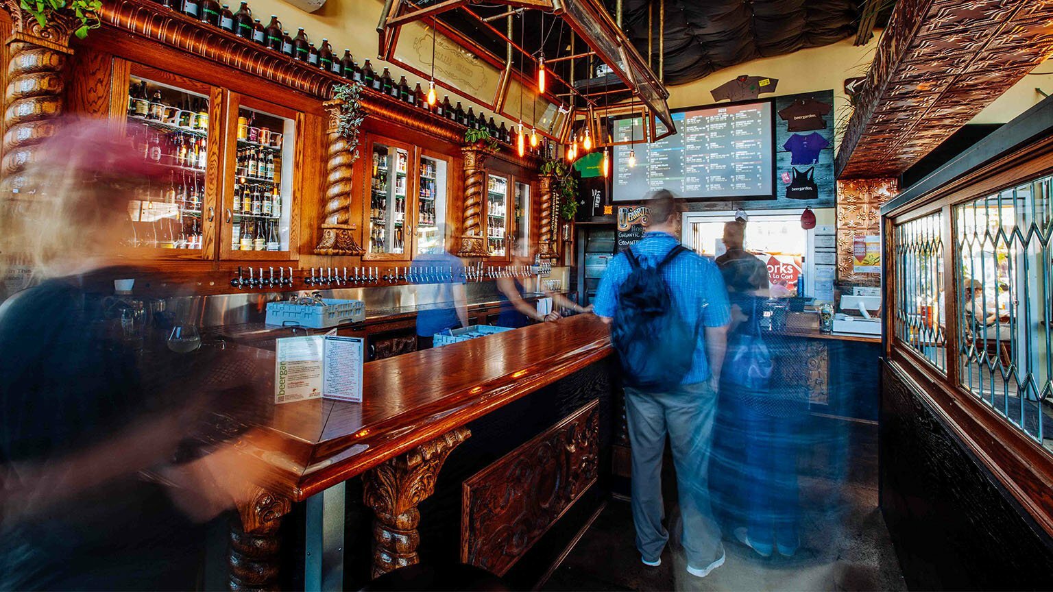 Busy bar interior with carved wood back bar, taps and patrons ordering, long-exposure motion blur