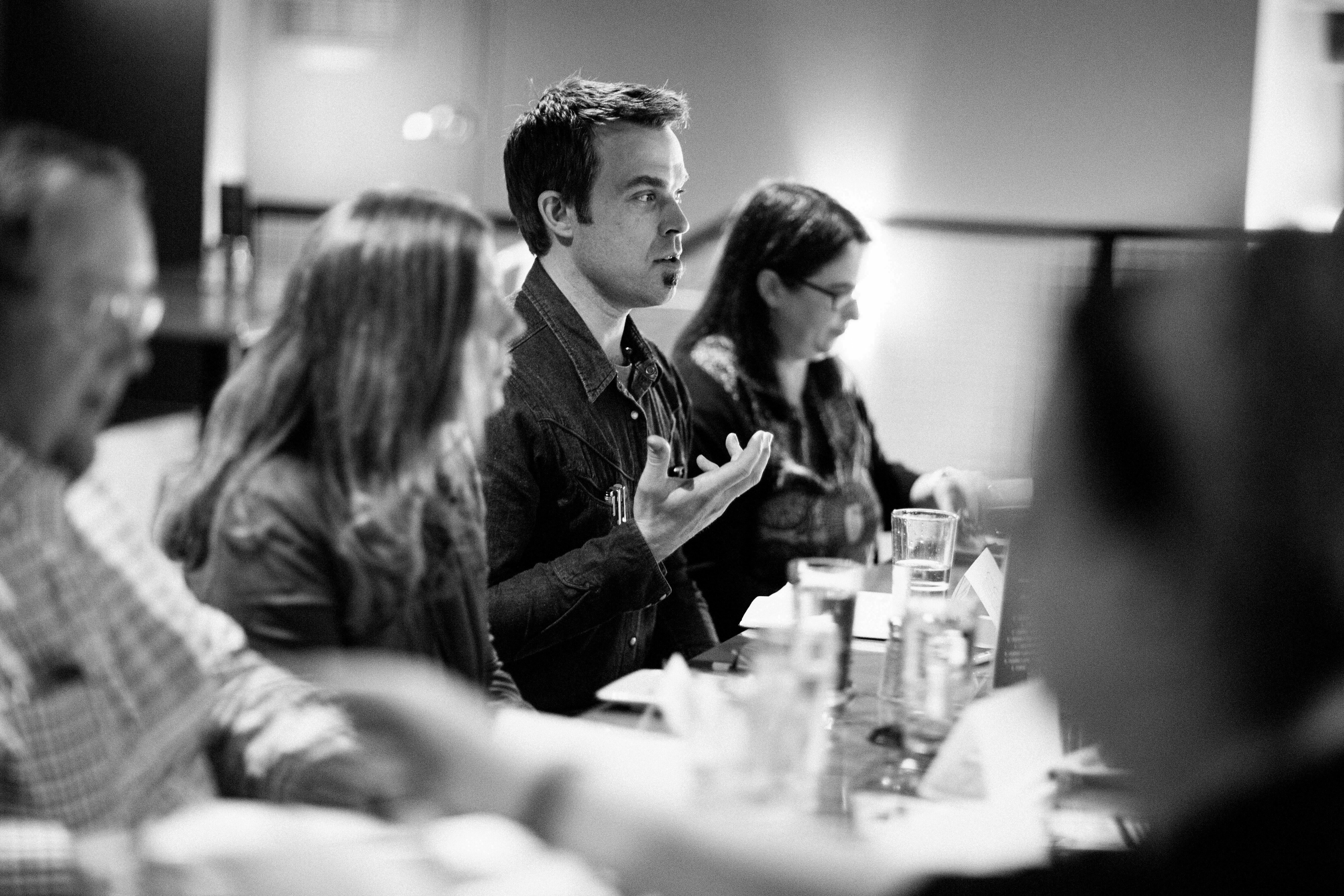 Man gesturing while speaking during a discussion at a table, black and white