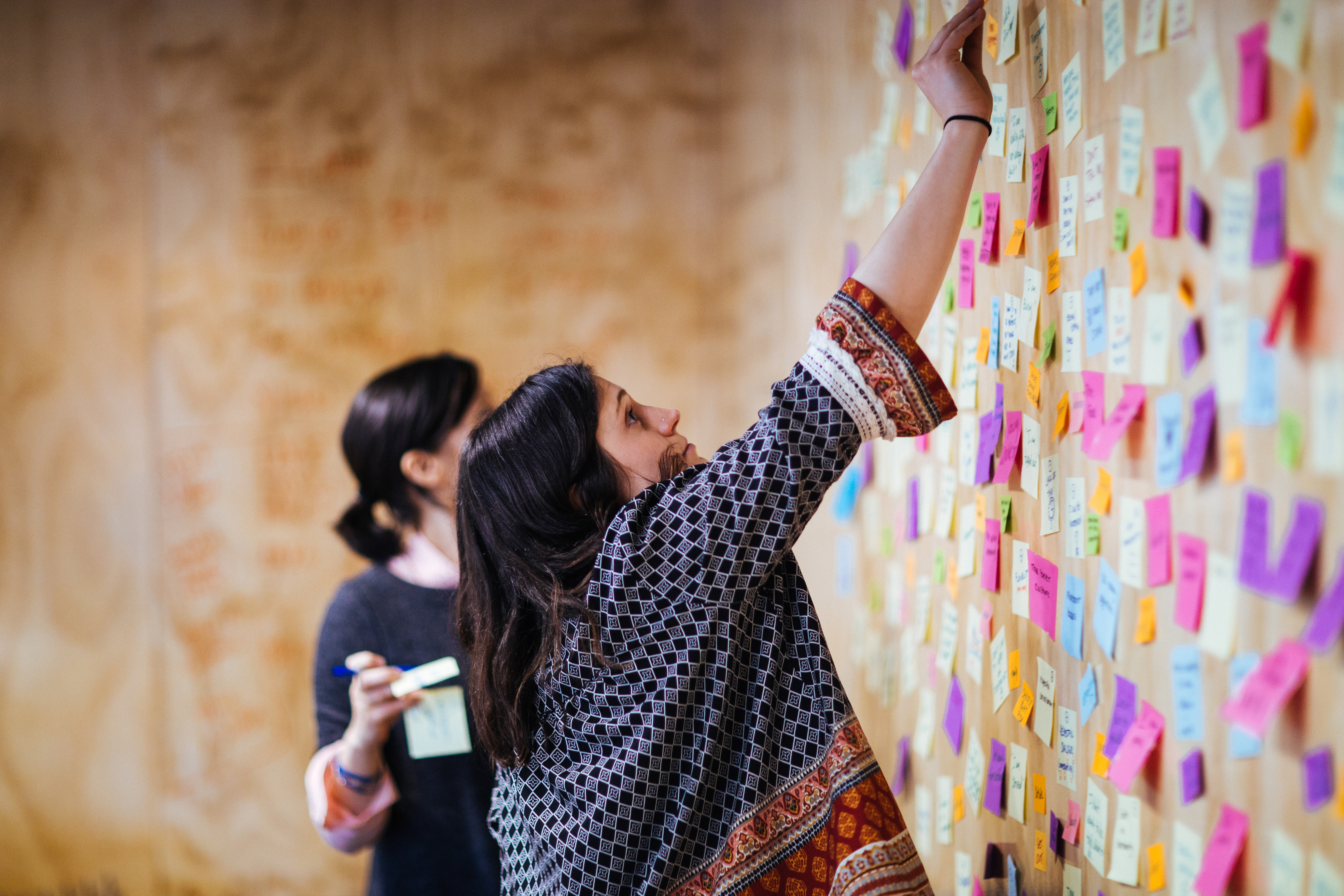 Woman placing a sticky note on a wall covered in colorful notes during a research workshop