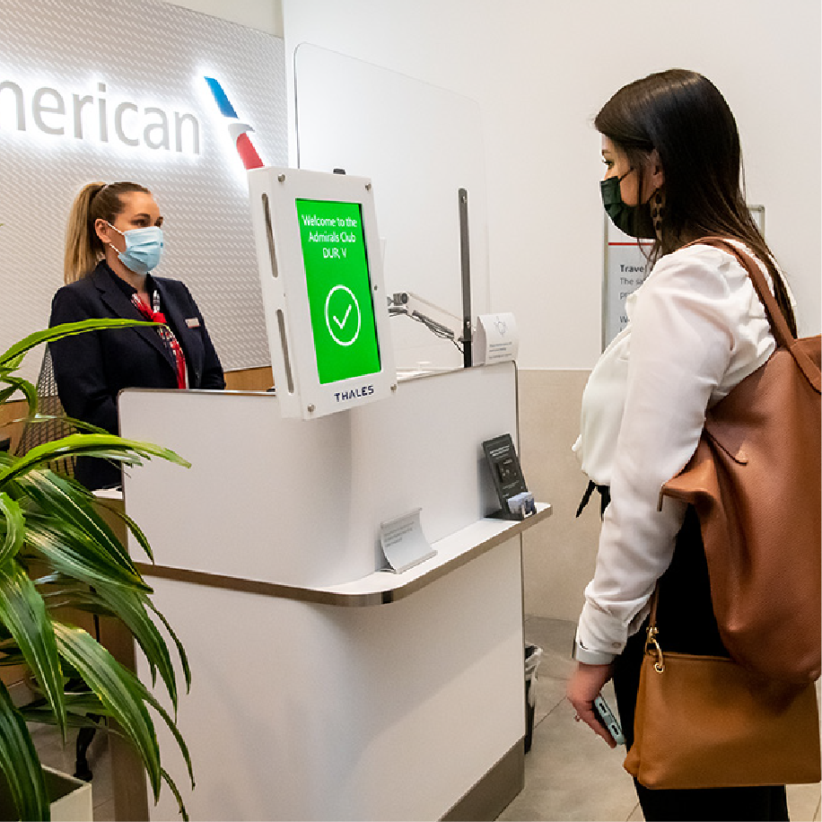 Traveler checks in at an American Airlines Admirals Club kiosk with a masked agent