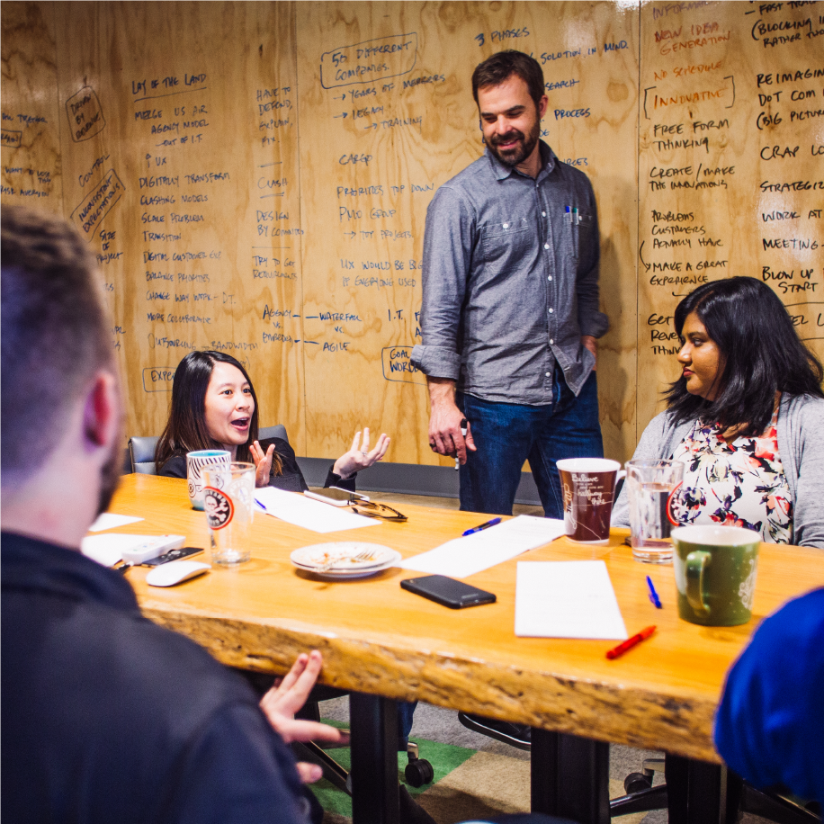 American Airlines workshop: facilitator leads a discussion at a table by a brainstorm-covered plywood wall