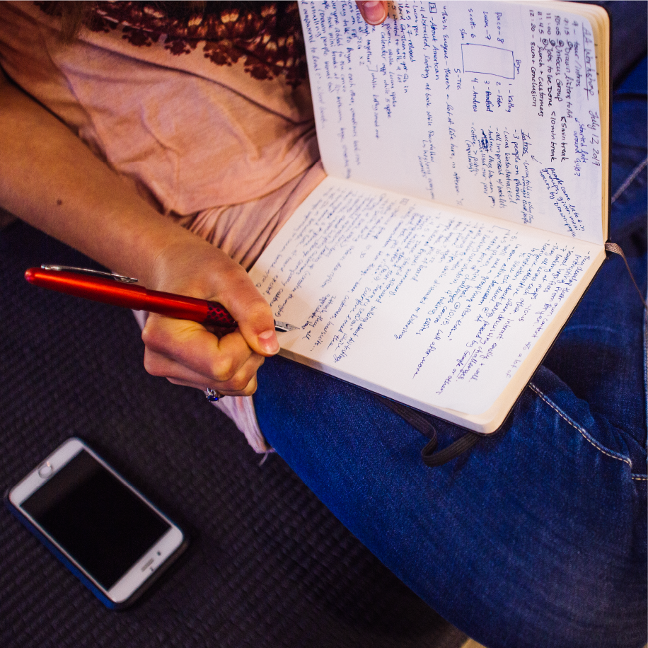Workshop participant takes handwritten notes in a notebook with a phone resting nearby