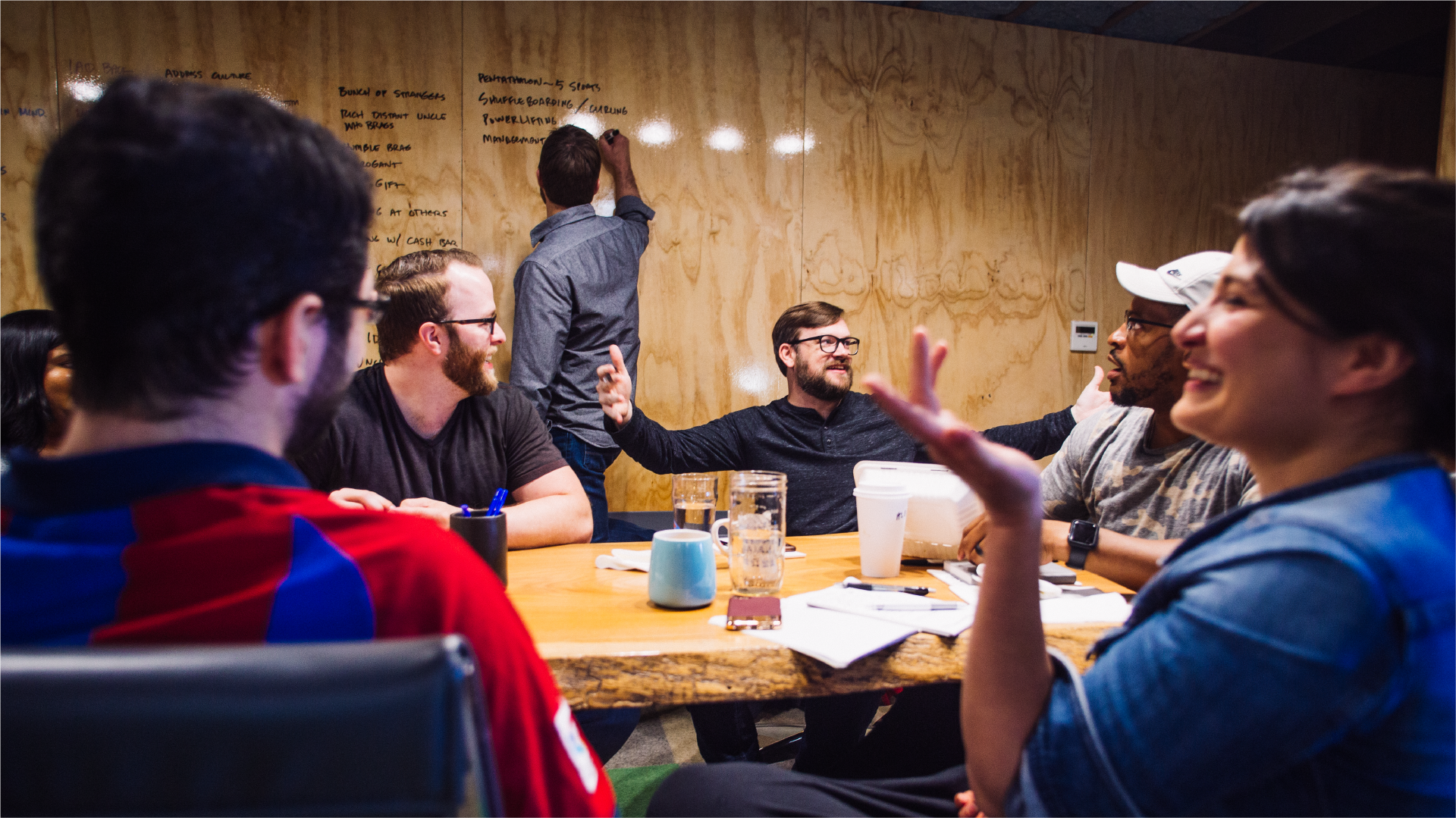 American Airlines design-thinking workshop: team at a table while a man writes ideas on a plywood wall