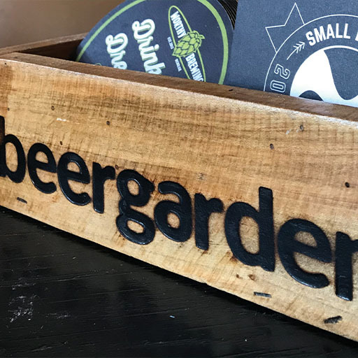 Wooden crate carved with the beergarden wordmark holding stacked screen-printed merchandise