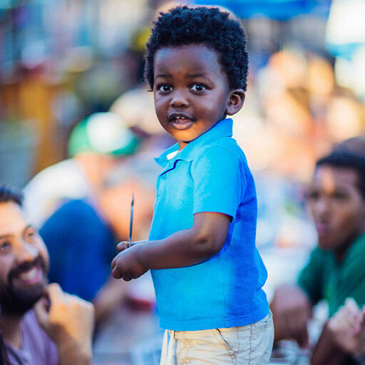 Toddler in a blue polo holding a straw amid smiling diners at the Beergarden food hall