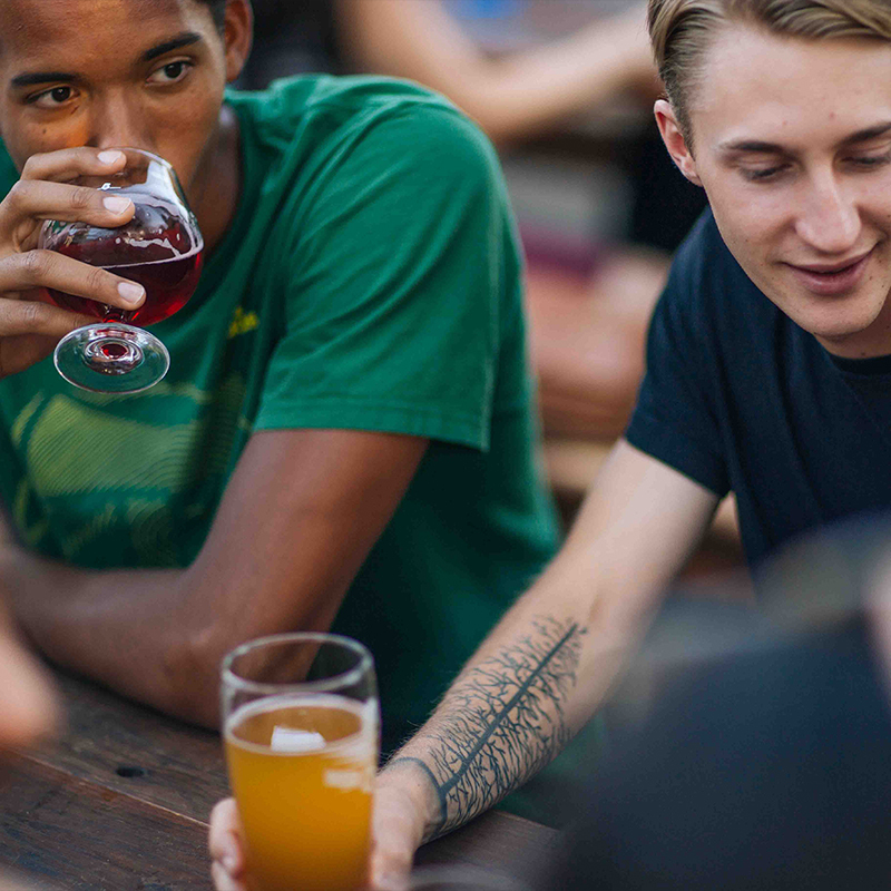 Two young men drinking craft beer at an outdoor wooden table at Beergarden in Eugene, Oregon