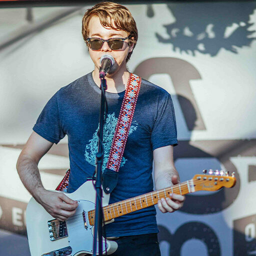 Young man in sunglasses singing and playing electric guitar on stage at Beergarden food hall