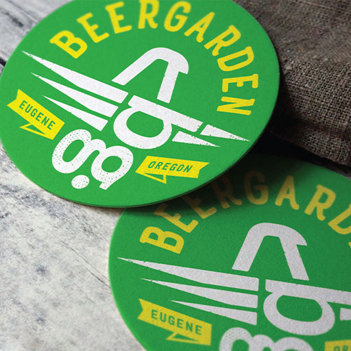 Green Beergarden Eugene Oregon coasters with white bird-and-glass logo on a wood surface