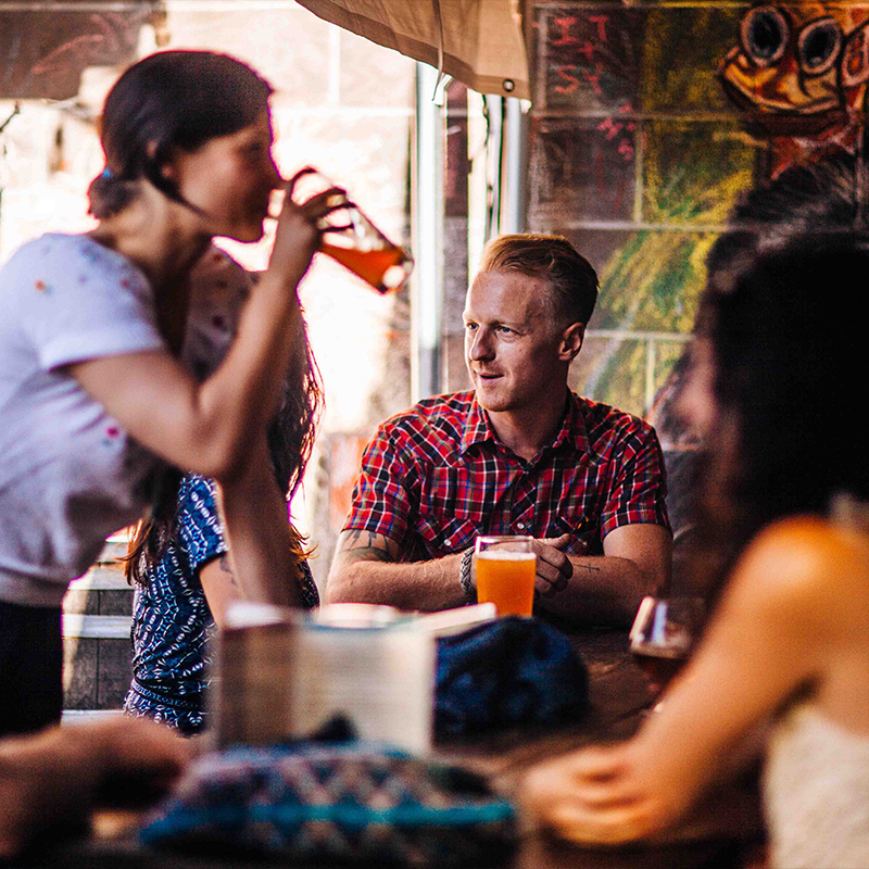 Friends drinking beer at a Beergarden patio table beside a chalk-art brick wall