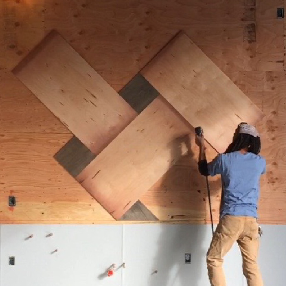 Person on a climbing wall installing angled plywood panels in a geometric diamond pattern