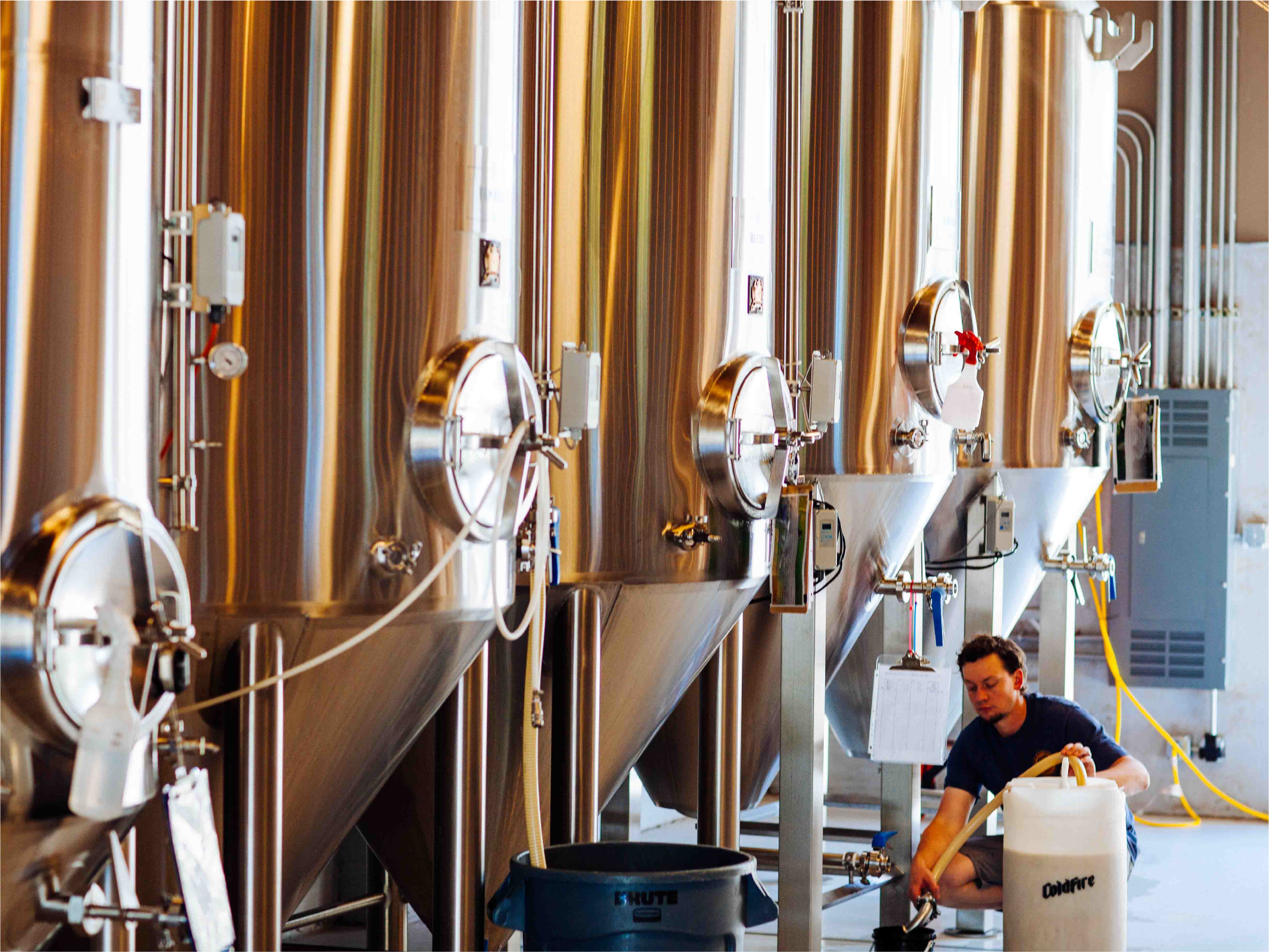 Worker tending rows of stainless steel ColdFire fermentation tanks in the brewery