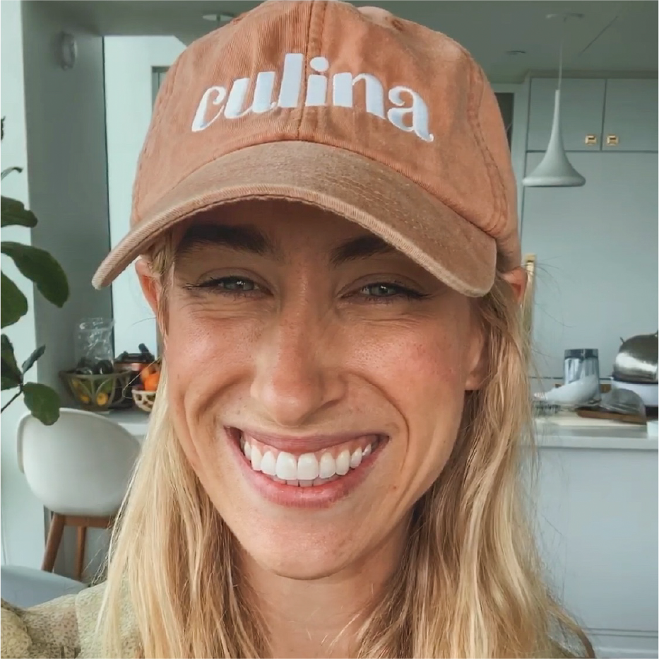 Smiling blond woman wearing a tan Culina baseball cap in a bright kitchen
