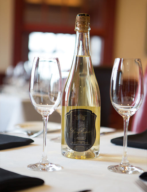 King Estate sparkling wine bottle and two empty glasses on a set restaurant table