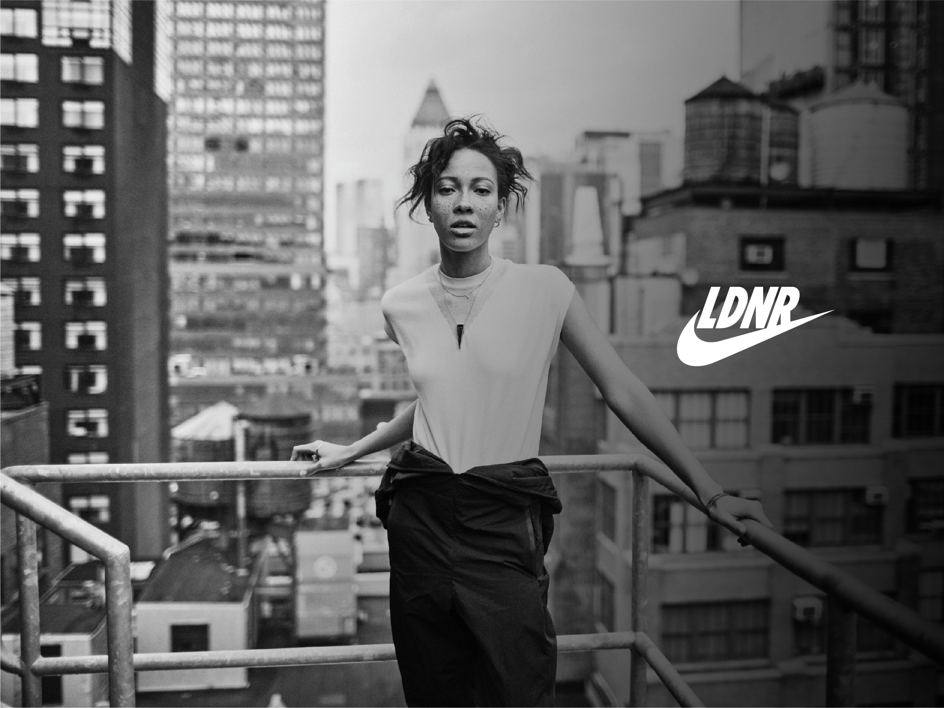 Black-and-white Nike LDNR ad of a woman on a rooftop railing against a city skyline