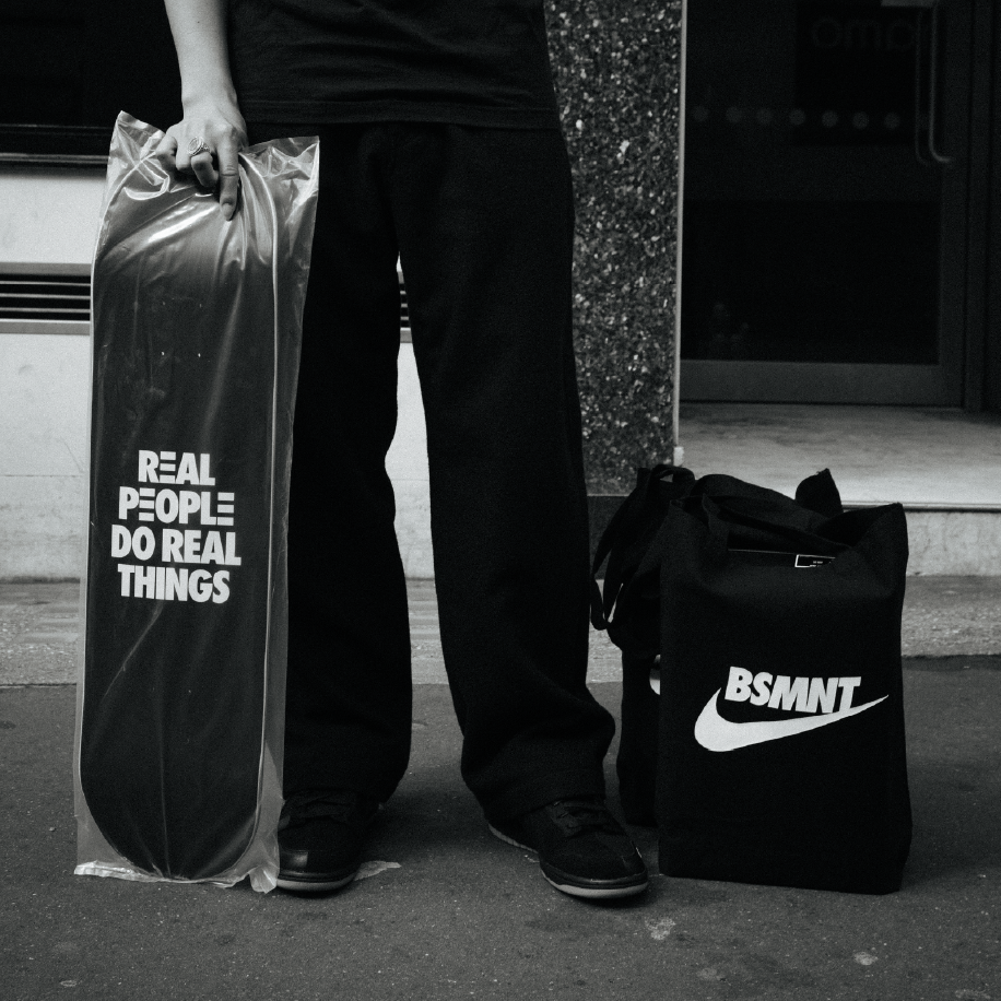 Nike London: person holding a wrapped skateboard and a BSMNT Nike tote bag on the street