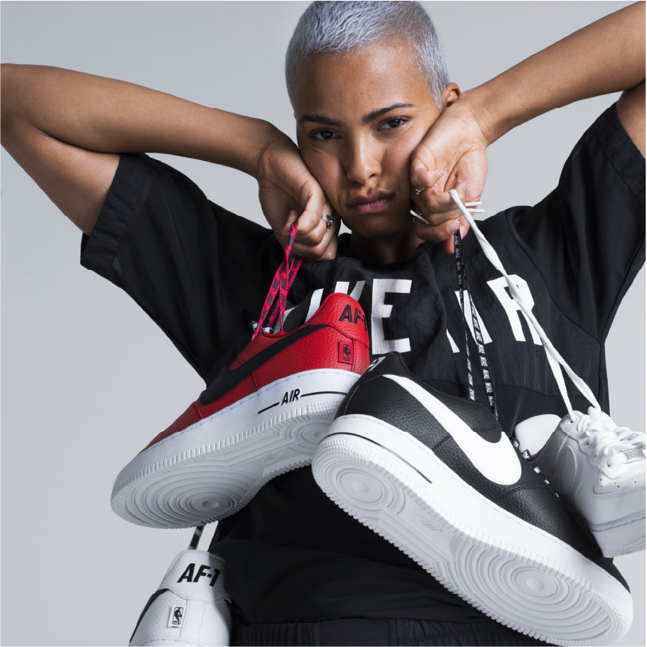 Woman in a Nike Air tee holds up red and black Air Force 1 sneakers by their laces, Nike London