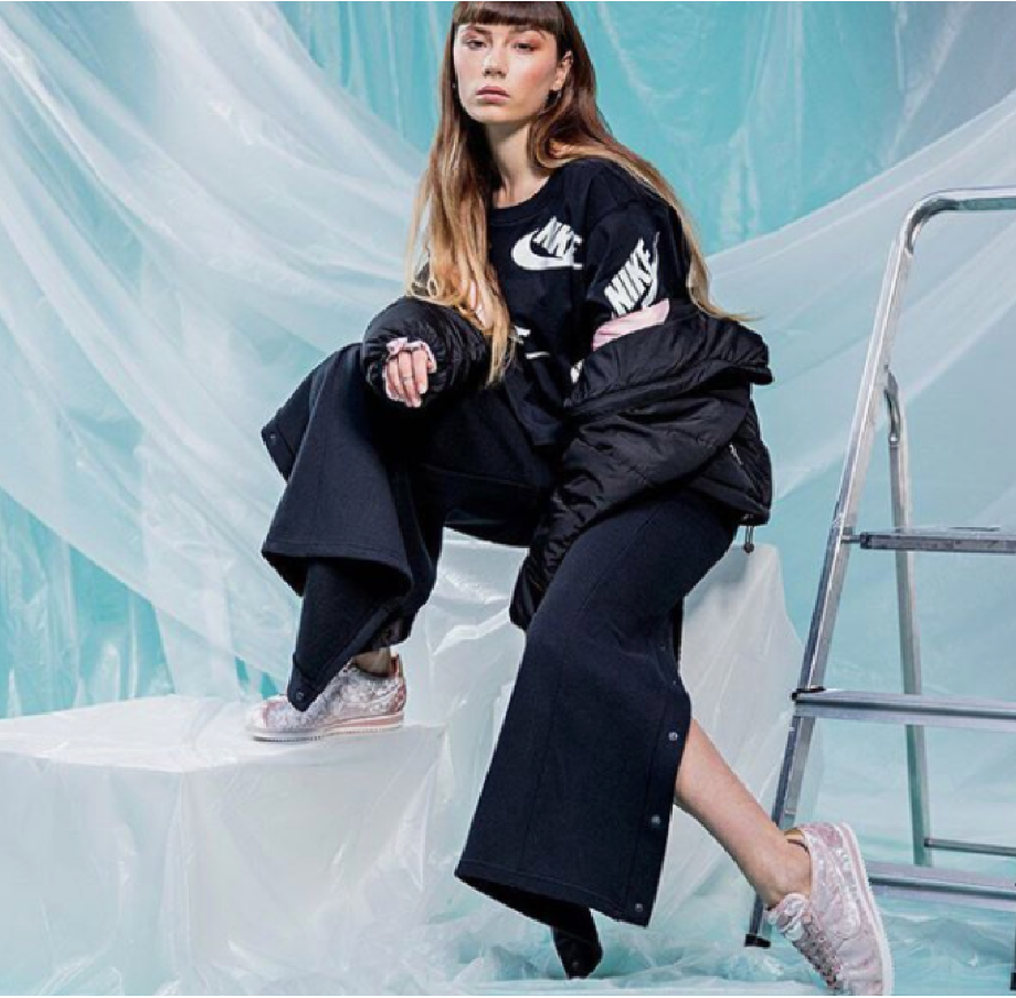 Woman in black Nike sportswear sits on a white block before an icy backdrop with a ladder, Nike London