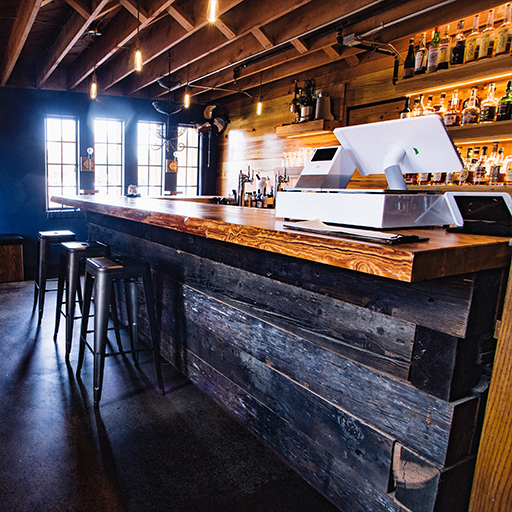 Reclaimed-wood bar with stools and tablet point-of-sale terminal inside Public House food hall