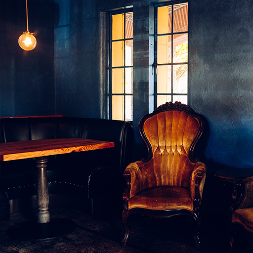 Moody Public House lounge with a velvet armchair, live-edge table and warm light by tall windows