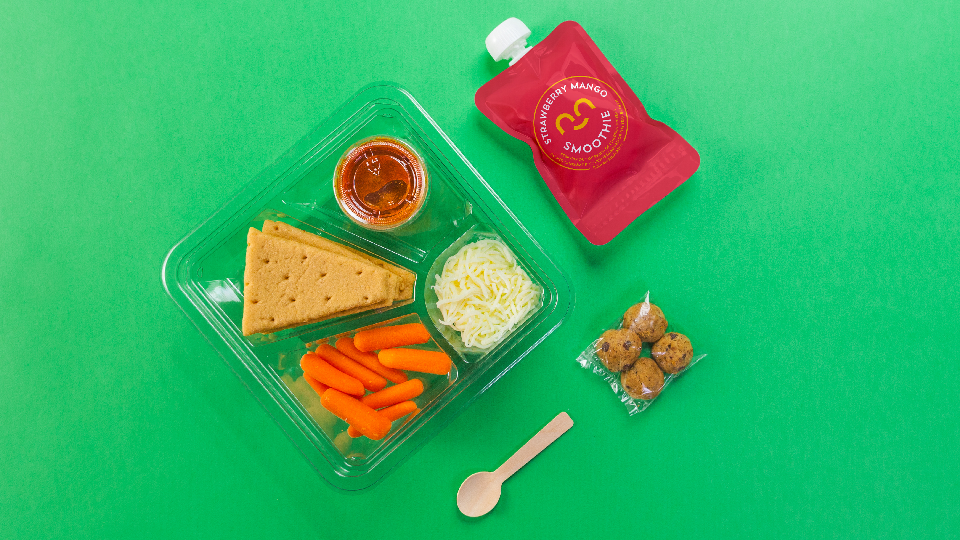 Sunnie lunch tray with crackers, carrots and cheese beside a Strawberry Mango smoothie pouch on green