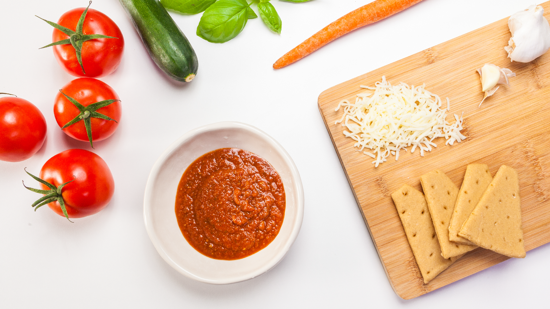 Sunnie pizza-kit ingredients: tomatoes, zucchini, carrot, basil, shredded cheese and crackers with sauce