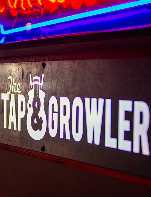 Illuminated The Tap & Growler sign on a wall with neon lights at the food hall
