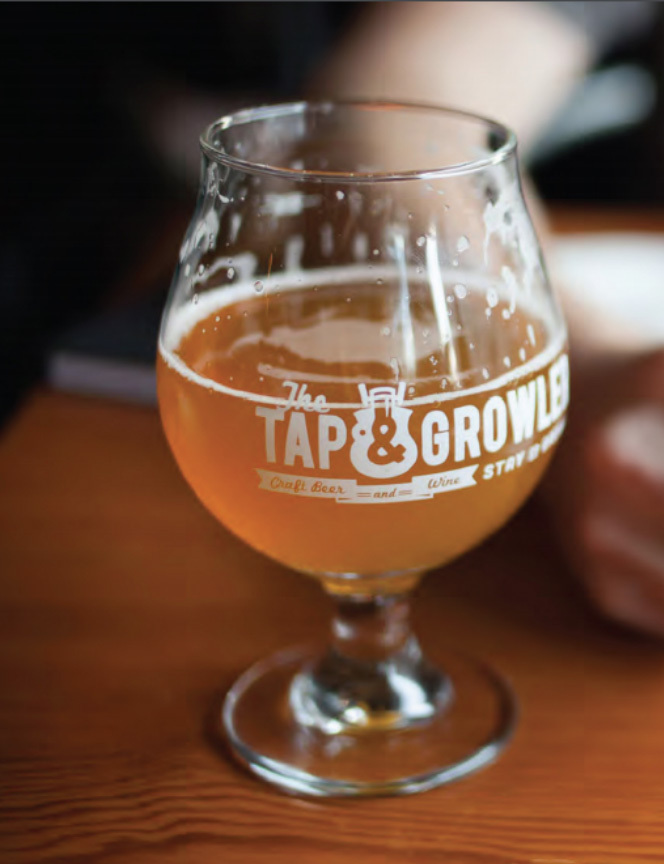 Patrons gathered at outdoor patio tables under a blue umbrella outside the Tap and Growler