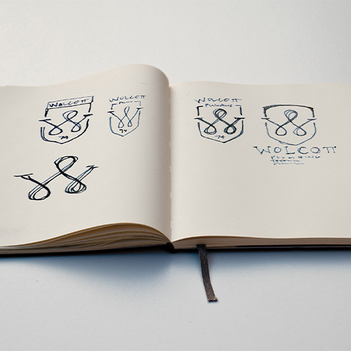 Open sketchbook with hand-drawn Wolcott shield logo concepts in pen