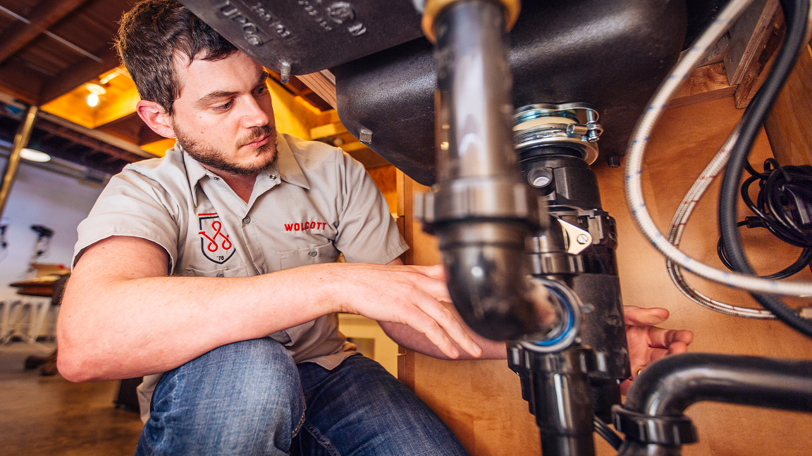 Wolcott plumber in branded shirt working on pipes under a sink