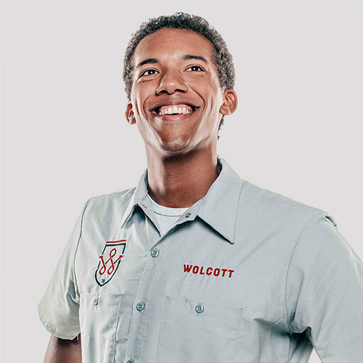 Young Wolcott technician laughing in grey uniform shirt with shield logo, recruitment portrait