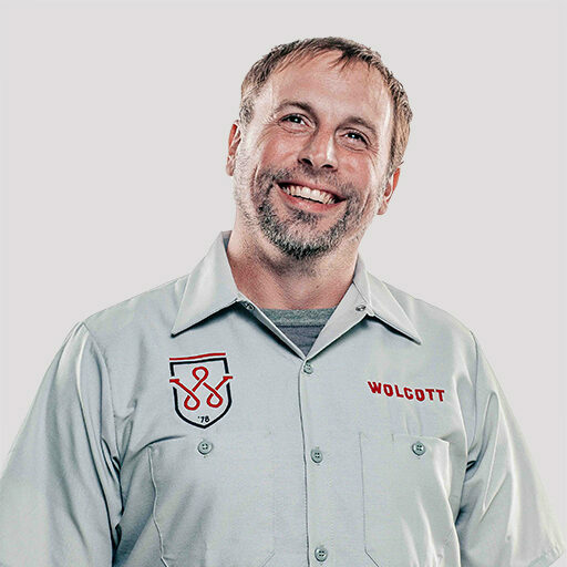 Smiling Wolcott tradesman in grey uniform shirt with shield logo, recruitment portrait