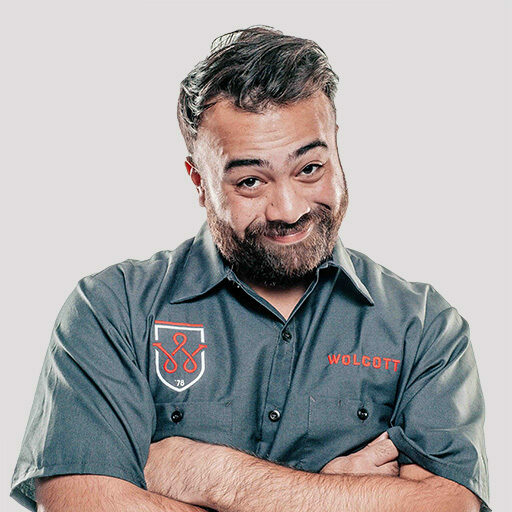 Bearded Wolcott worker in grey uniform shirt with shield logo, arms crossed, recruitment portrait