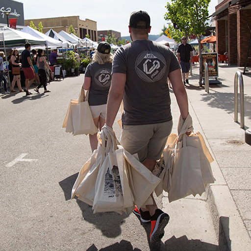 Two people in Let's Co tees carry tote bags through an outdoor farmers market, WSECU campaign