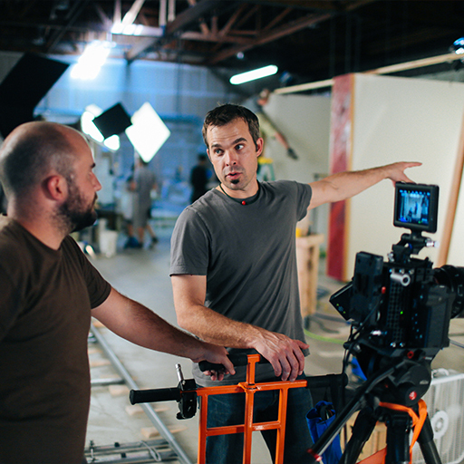 Two crew members talk beside a cinema camera on a WSECU video shoot in a lit warehouse