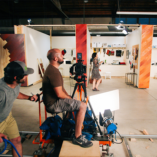 WSECU ad shoot: crew films an actor riding a camera dolly inside a warehouse set with colorful wood panels