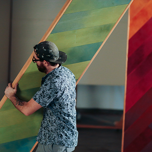 Man in cap carries a tall rainbow-striped wooden panel for the WSECU set design