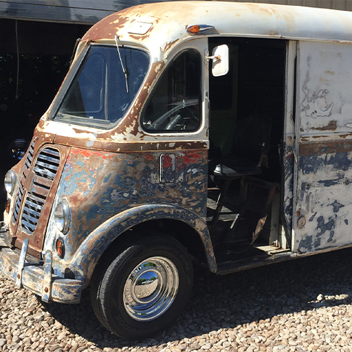 Rusty unrestored vintage step van with open side door parked on gravel, WSECU Let's Co build
