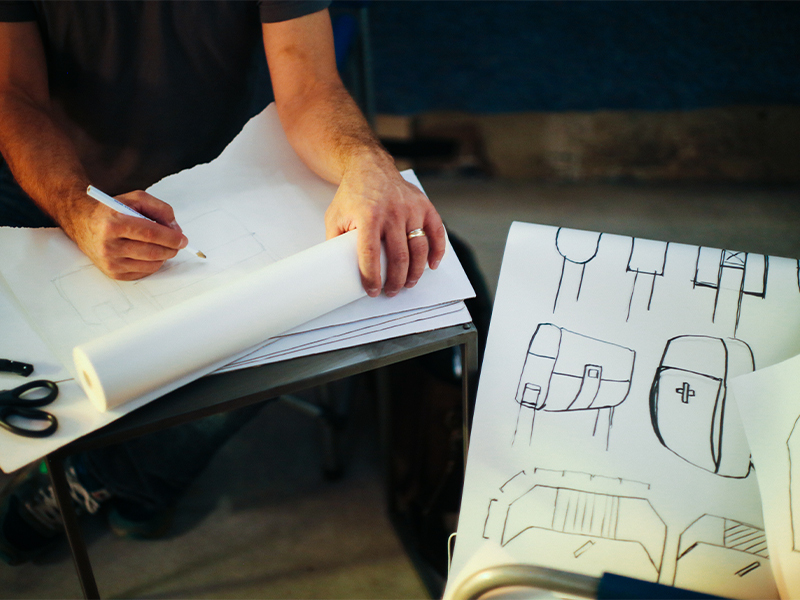 Designer sketching bag and product concepts on paper at a workbench, WSECU design fabrication