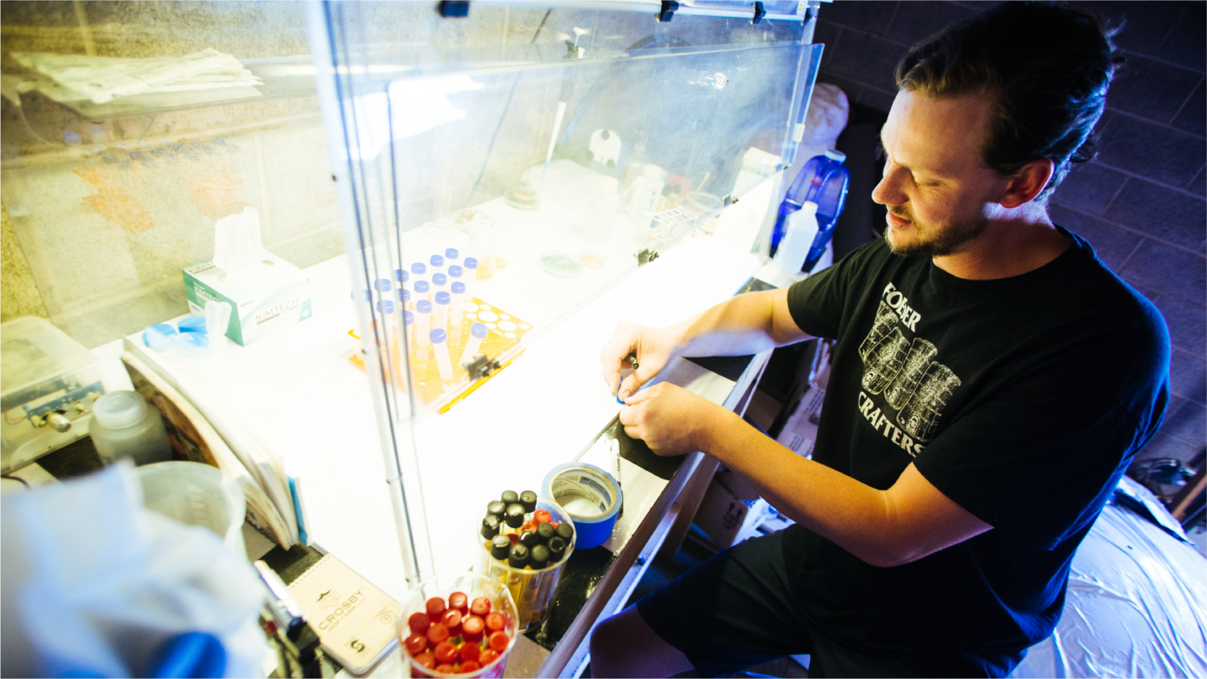 ColdFire brewer working at an illuminated lab cabinet with trays of fruit and culture jars