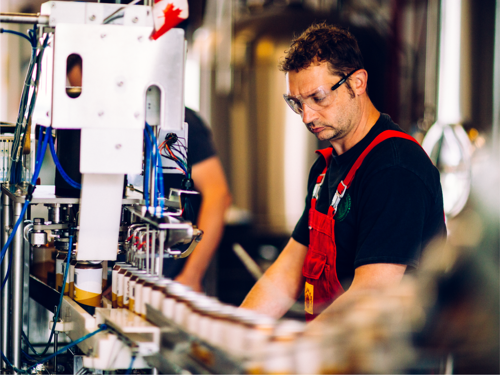 ColdFire worker in safety glasses and red apron operating the bottling line in the brewery
