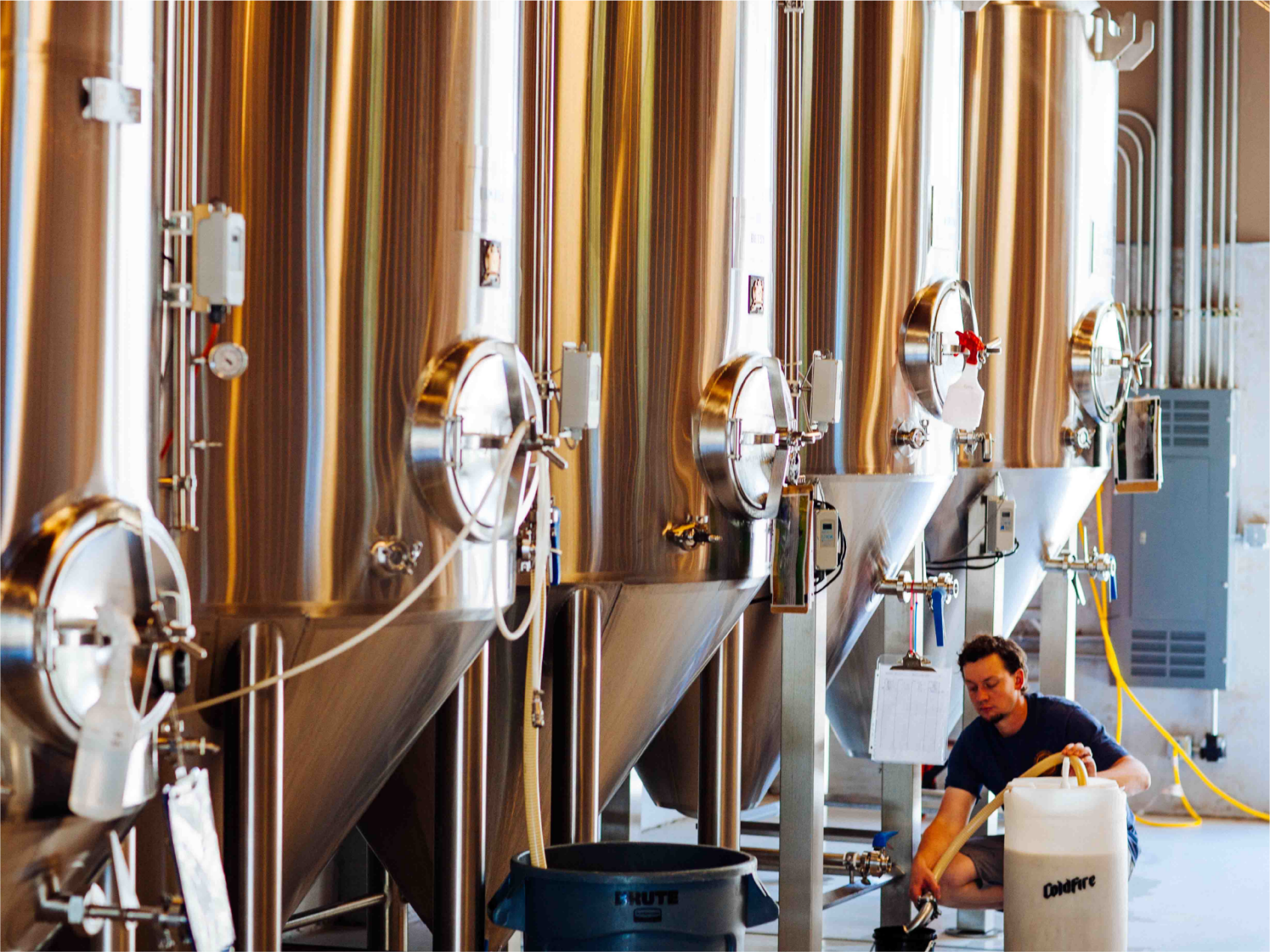 Worker tending rows of stainless steel ColdFire fermentation tanks in the brewery