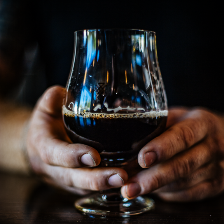 Hands cradling a snifter of dark ColdFire beer against a black background