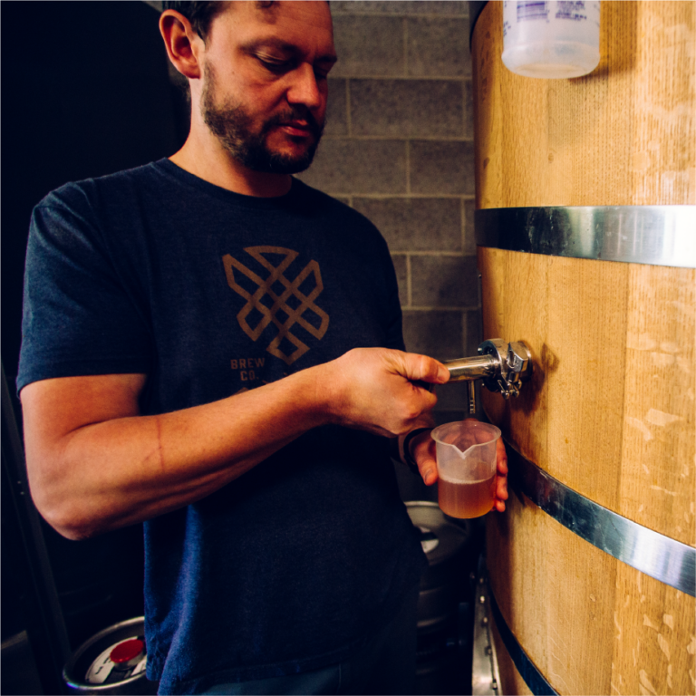 ColdFire brewer in a logo tee pouring beer from a barrel spigot into a clear cup
