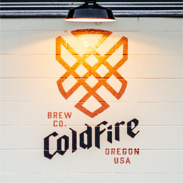 ColdFire Brew Co. Oregon USA wordmark and emblem painted on a wall lit by a hanging lamp