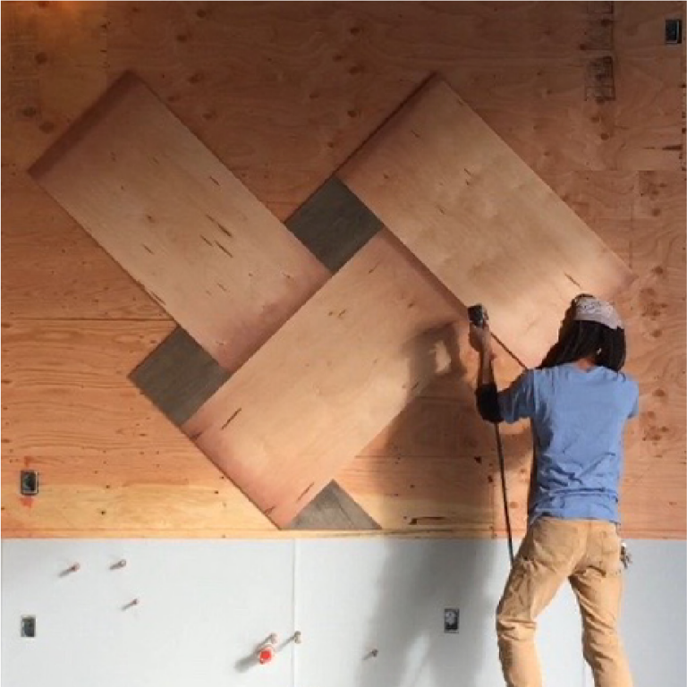Person on a climbing wall installing angled plywood panels in a geometric diamond pattern