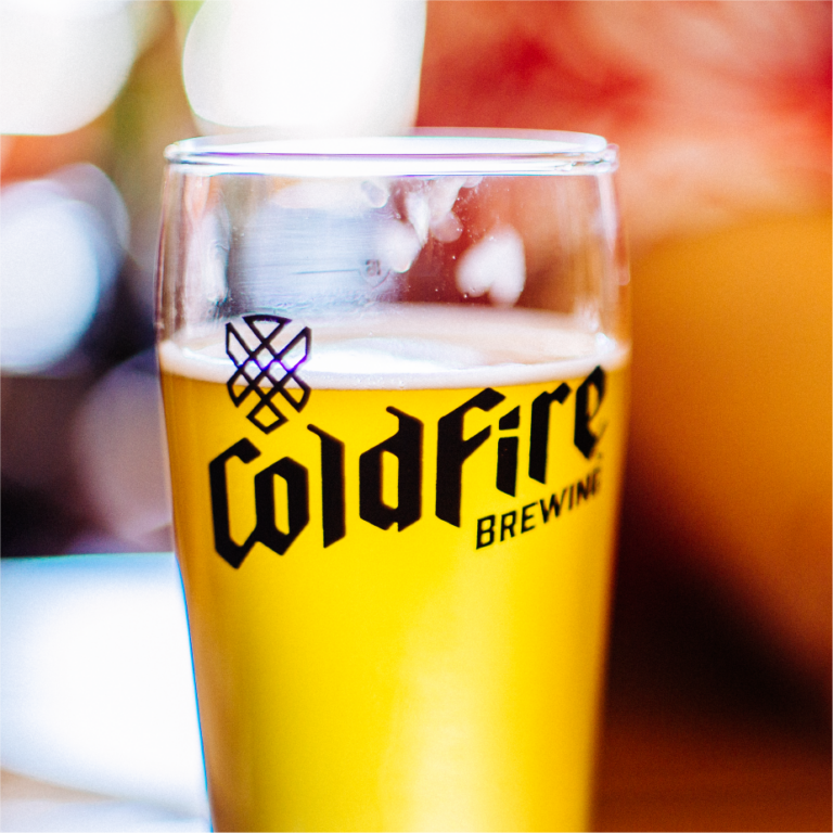 Close-up of a glass of beer with the black ColdFire Brewing logo and hop emblem