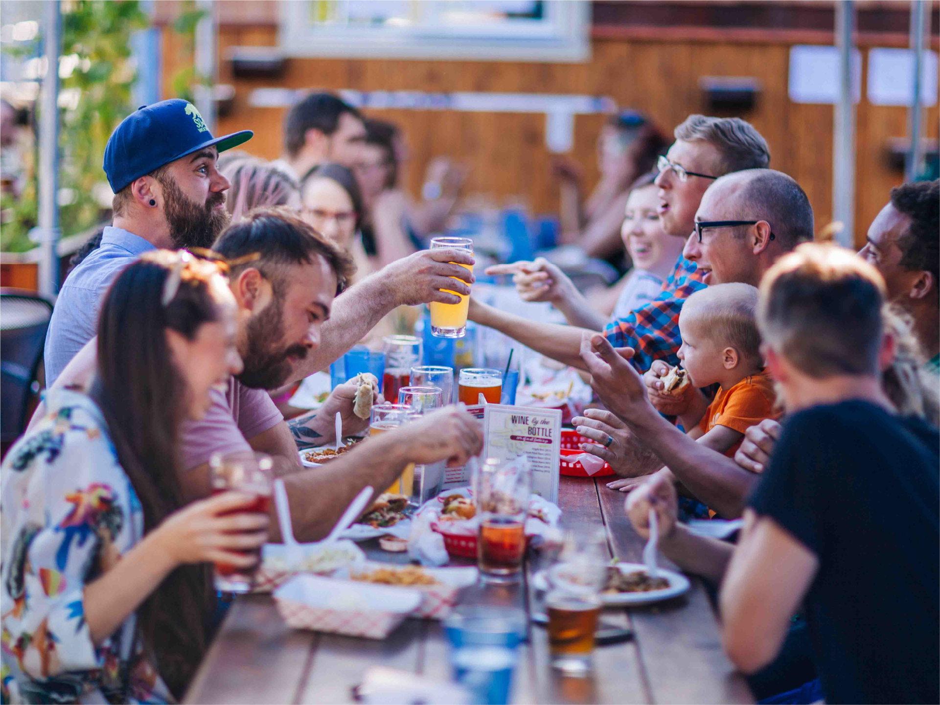 Friends toasting and sharing food and drinks at a crowded long outdoor table