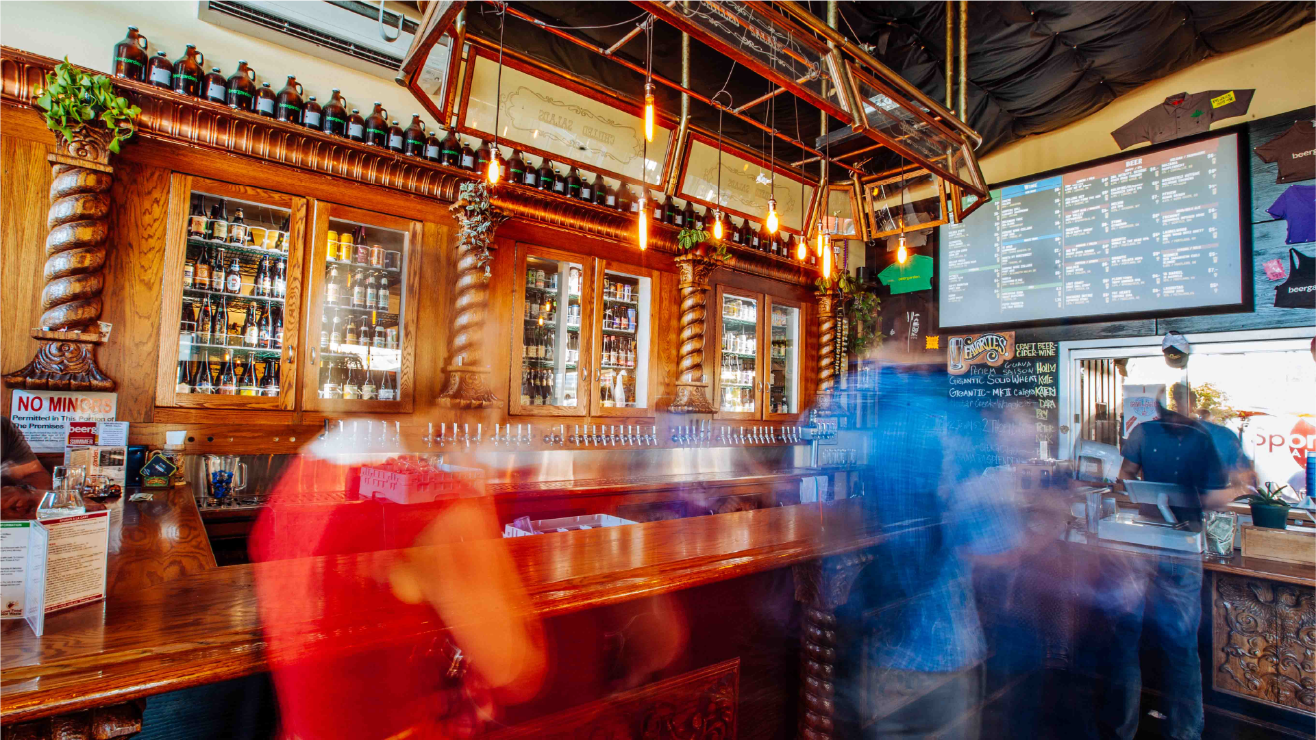 Interior of a busy bar with wood back-bar shelves, hanging lights and motion-blurred patrons