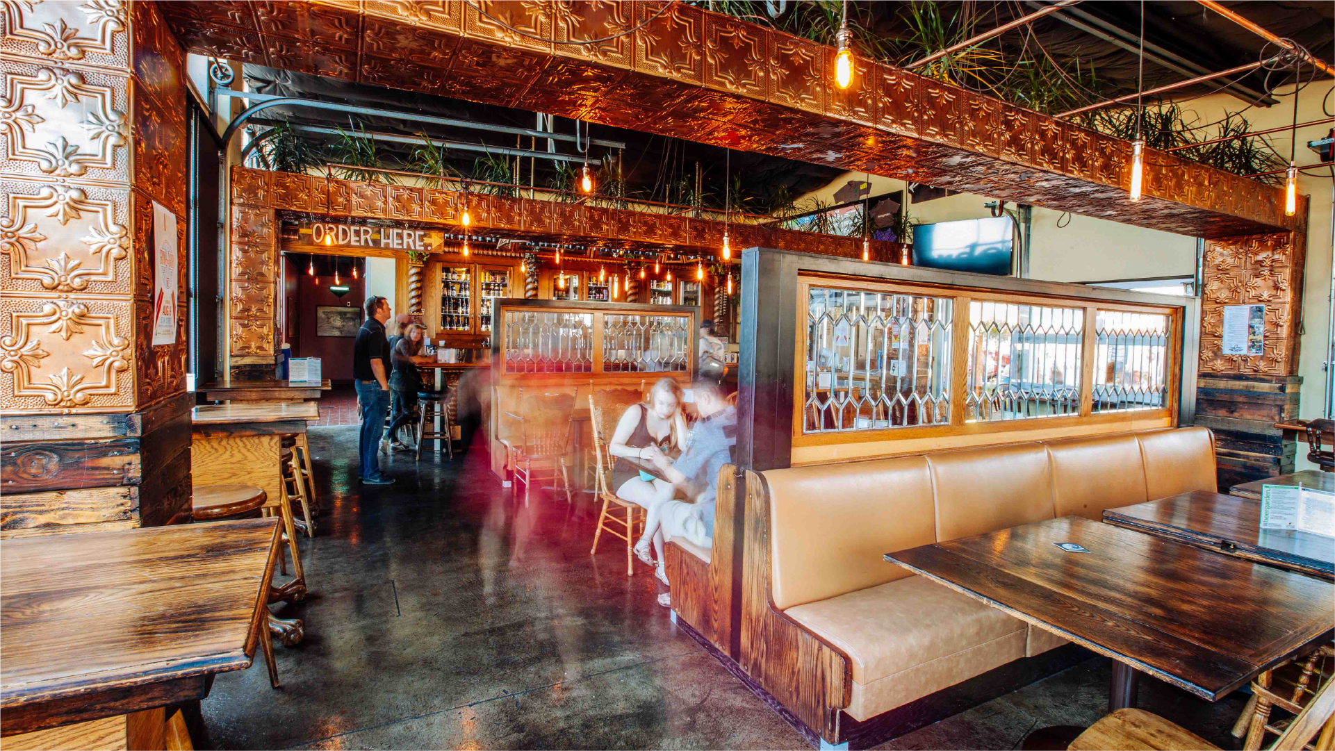 Interior of a brewery taproom with pressed-tin ceiling, Order Here sign and leather booth seating